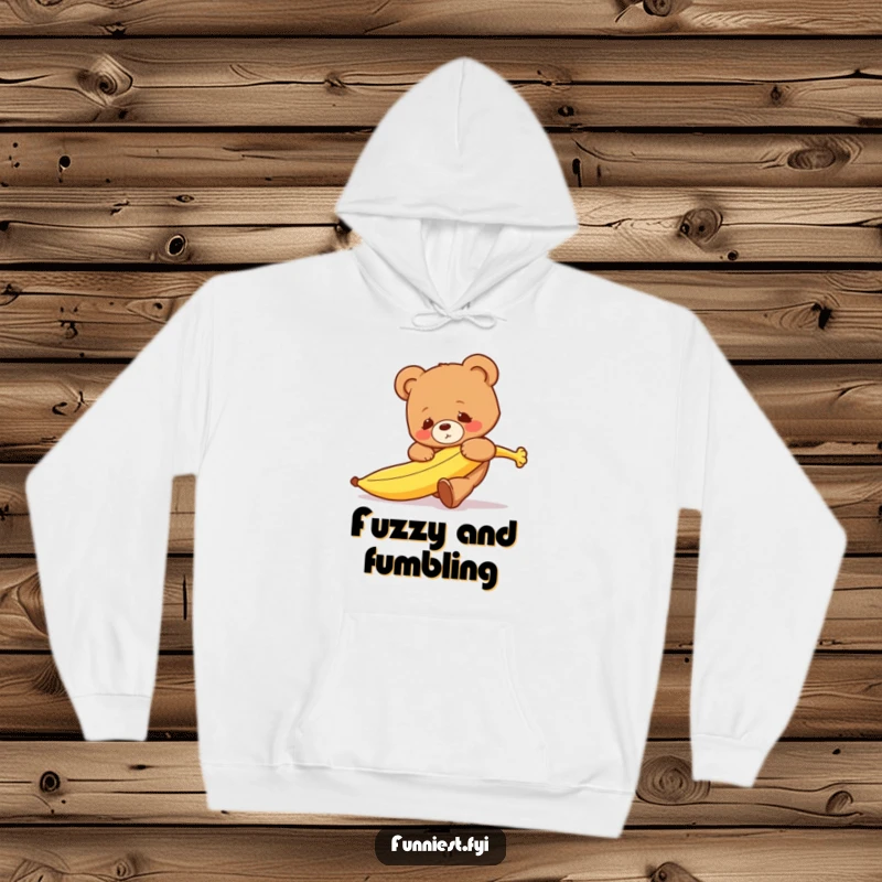 A cozy hoodie featuring a clumsy teddy bear character hilariously tripping over a runaway banana with a surprised expression.