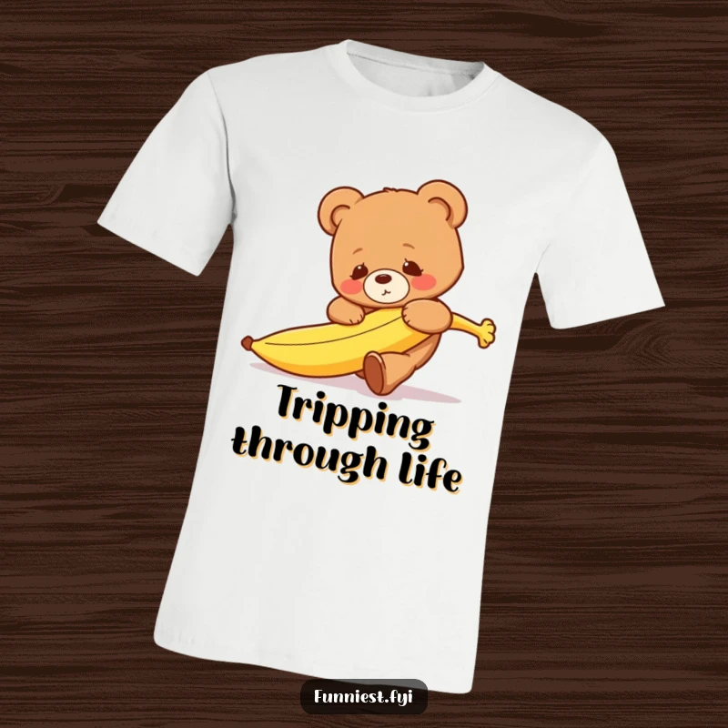 A funny, clumsy teddy bear character caught mid-trip over a runaway banana on this humorous t-shirt.